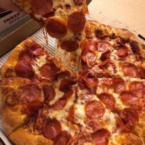 a pepperoni pizza being lifted from a box by a person holding a spatula