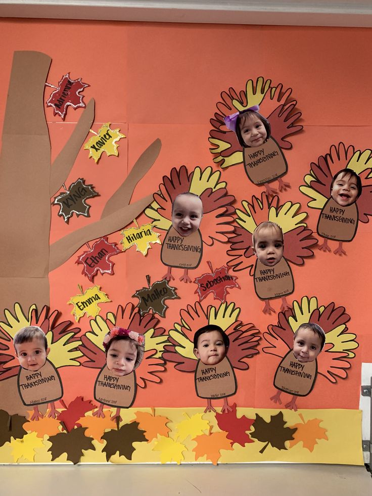 a bulletin board with pictures of children's faces and leaves on it in front of a tree