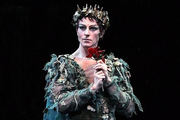 a woman dressed in costume holding a rose and looking at the camera while standing on stage