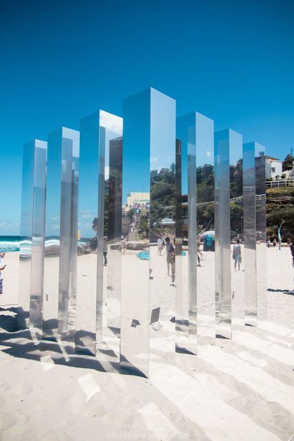 people are walking on the beach near large glass sculptures