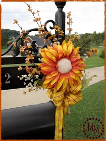 an orange and yellow sunflower tied to a light post in front of a black mailbox