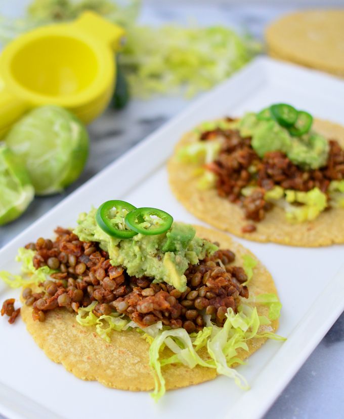 two tacos on a white plate with lettuce and other food items around them