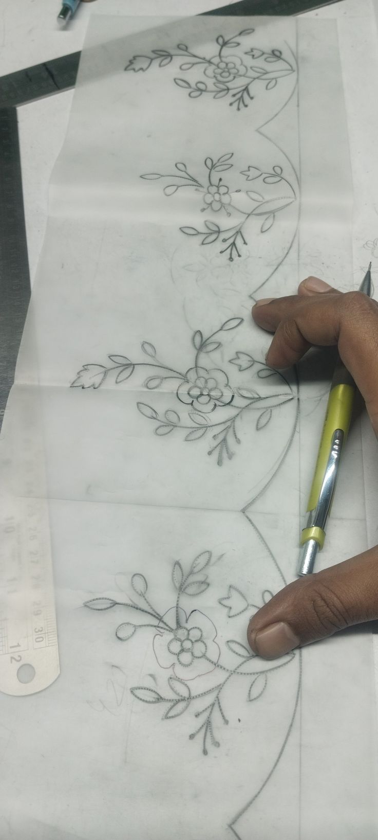 someone is drawing flowers on paper with a marker and pen in their left hand, while another person holds a pencil near the edge of it