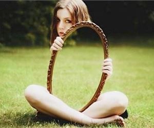 a woman sitting in the grass holding a snake around her neck