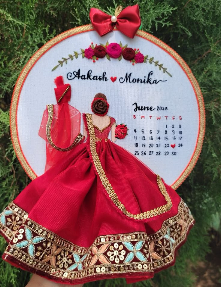 a hand holding a red doll in front of a calendar