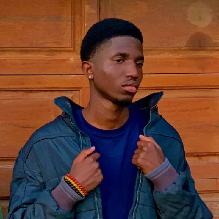 a young man is standing in front of a wooden wall