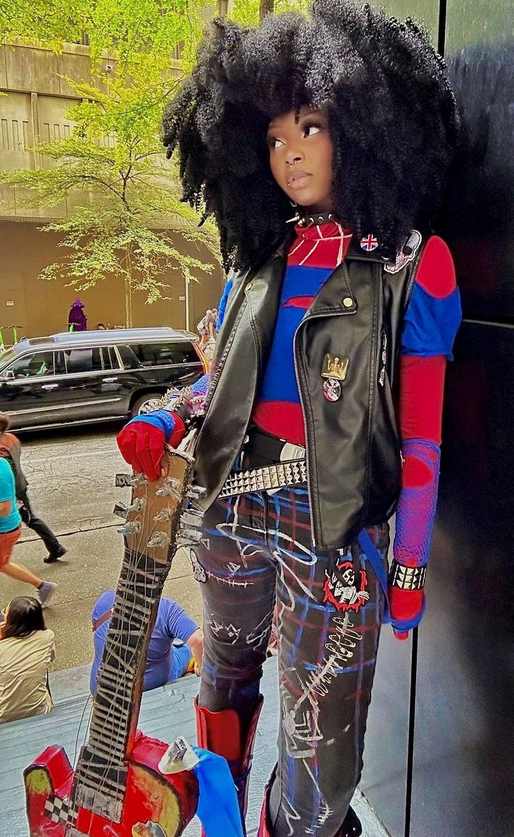 a woman with an afro holding a guitar on the sidewalk in front of a building