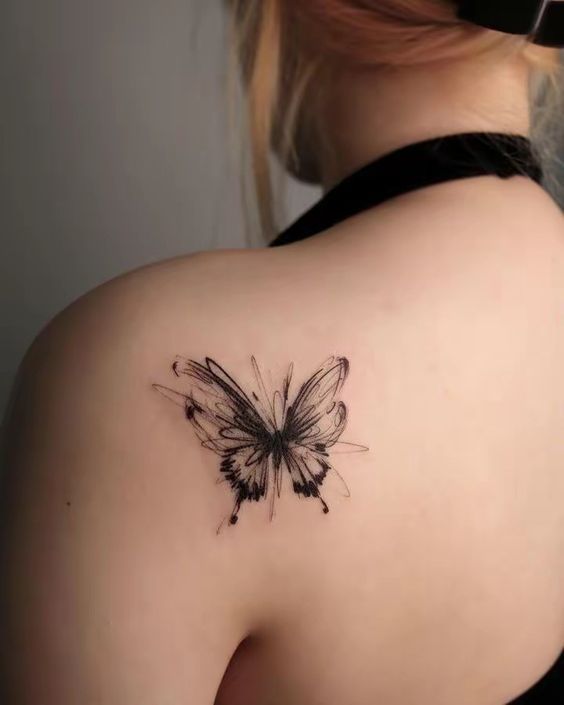 the back of a woman's shoulder with a black and white butterfly tattoo on it