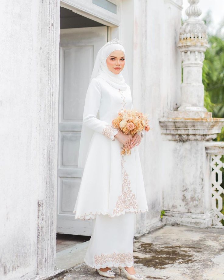 a woman wearing a white hijab holding a bouquet of flowers in her hands