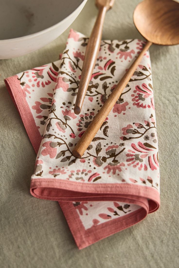 two wooden spoons sitting on top of napkins next to a bowl and utensils