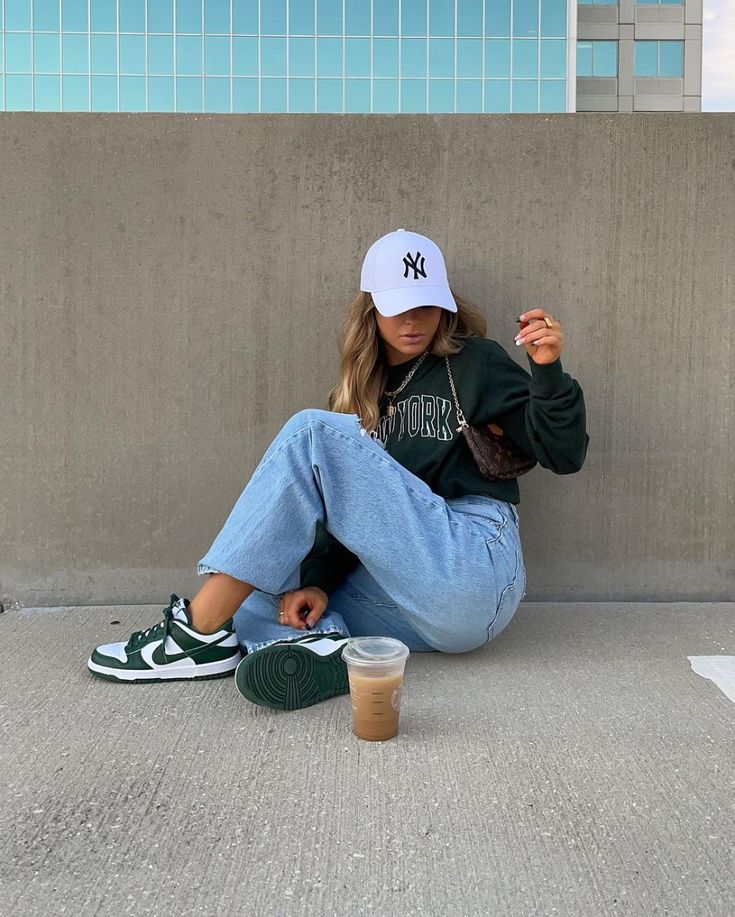 a young woman sitting on the ground with her feet up and holding a drink in one hand