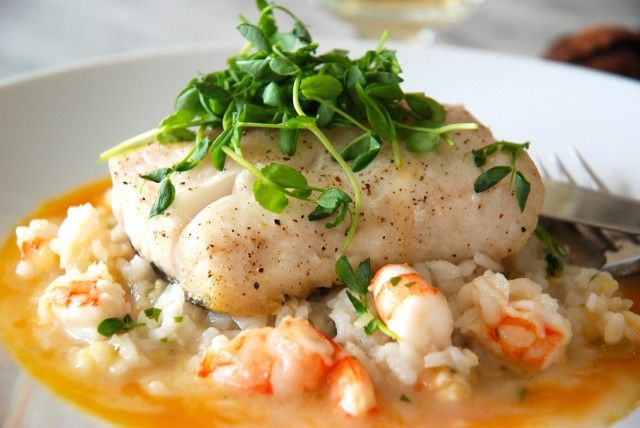 a white plate topped with rice covered in shrimp and garnished with green leaves