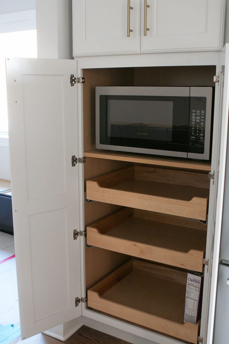 a microwave is open in a kitchen with white cupboards and wood flooring on the side