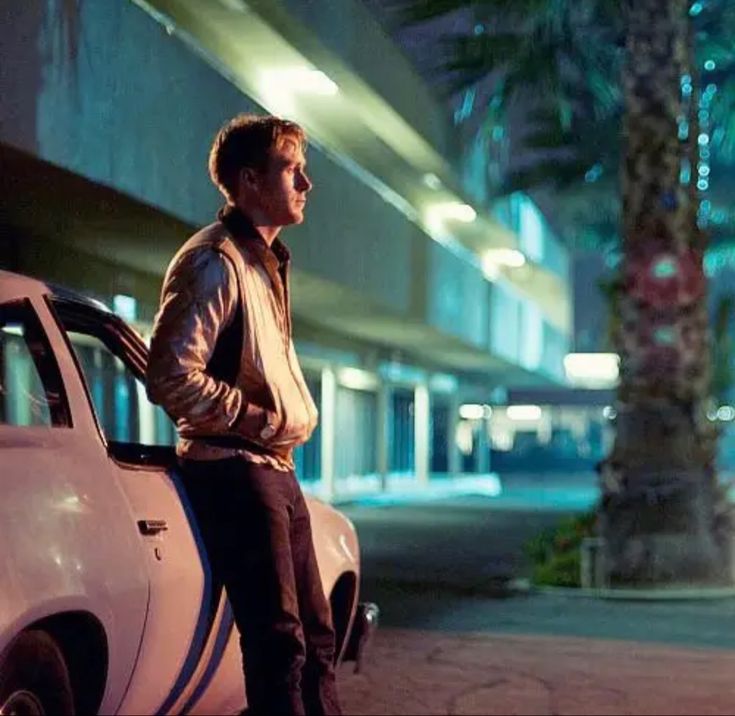 a man standing next to a white car on the side of a street at night