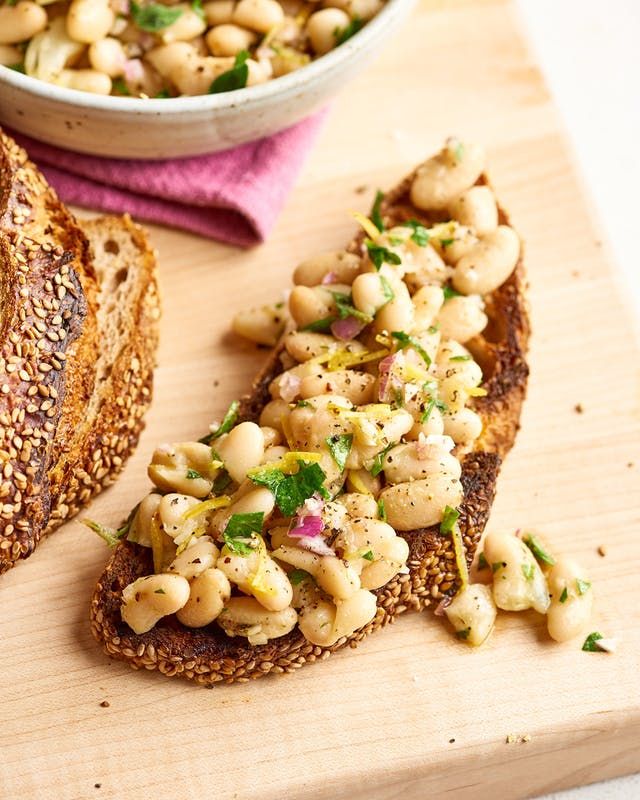 two pieces of bread with beans and herbs on them next to a bowl of soup