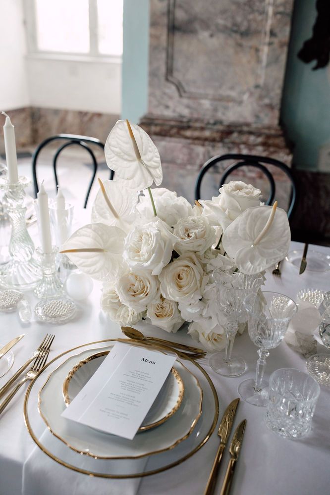 the table is set with white flowers and gold place settings