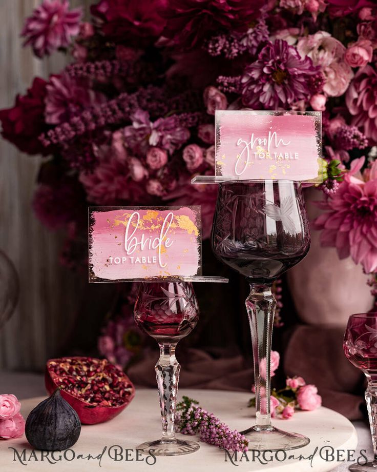 two wine glasses sitting next to each other on a table with flowers in the background