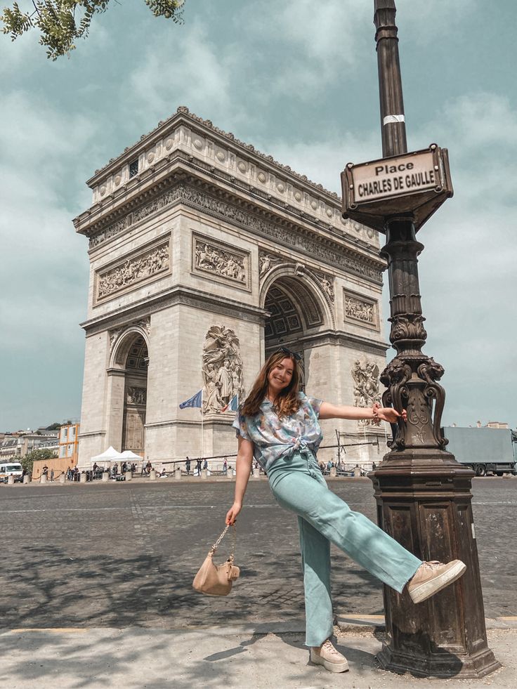 a woman leaning on a lamp post in front of the arc de trioe