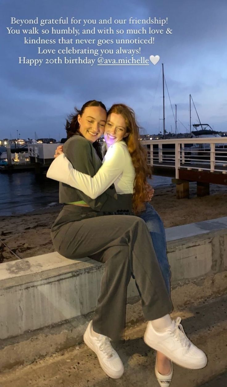 two women sitting on the edge of a pier with their arms wrapped around each other