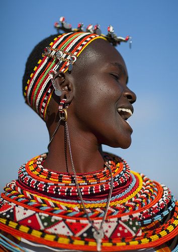 an african woman with colorful jewelry on her head and necklaces around her neck, smiling