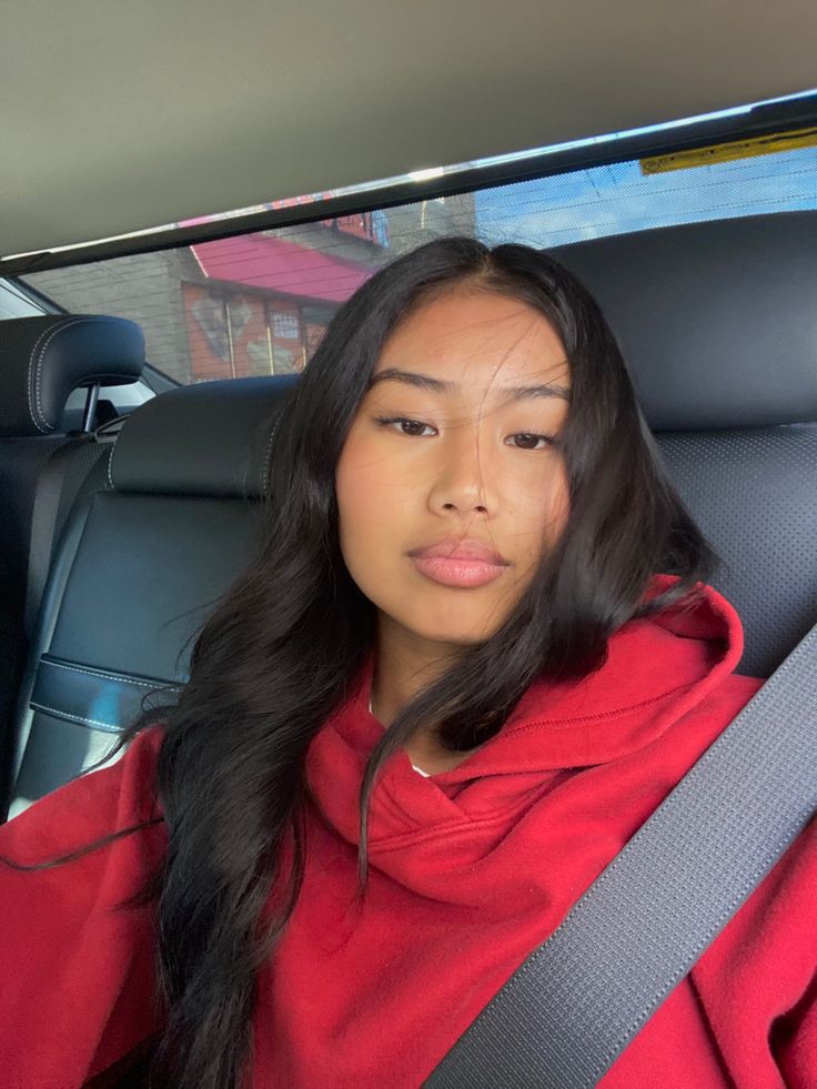 a woman sitting in the back seat of a car wearing a red hoodie and looking at the camera