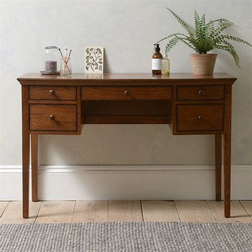 a wooden desk sitting on top of a hard wood floor next to a potted plant