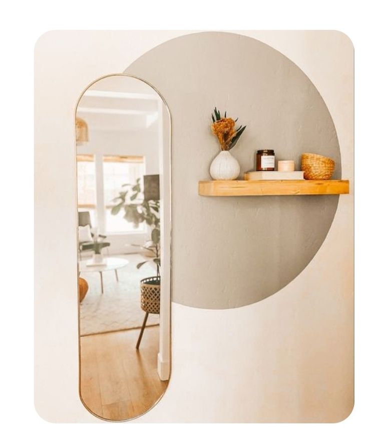 an oval shaped mirror hanging on the wall next to a shelf filled with vases