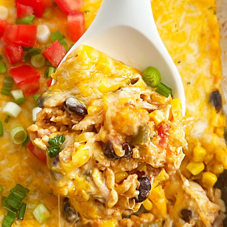 a spoon full of mexican chicken casserole with corn and tomatoes on the side