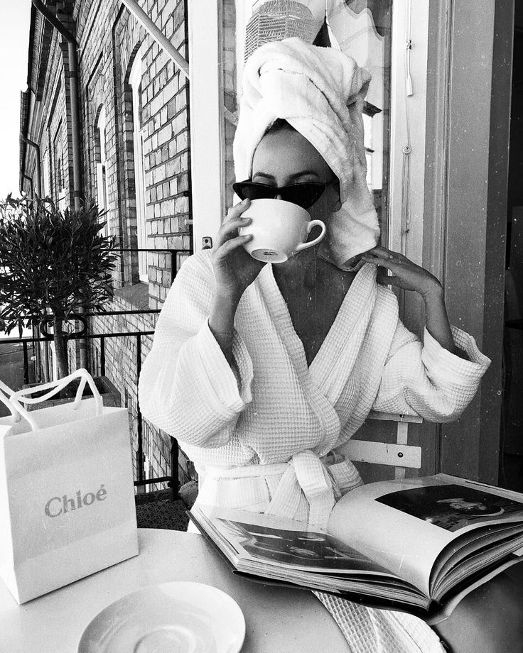 a black and white photo of a woman in a robe drinking from a coffee cup