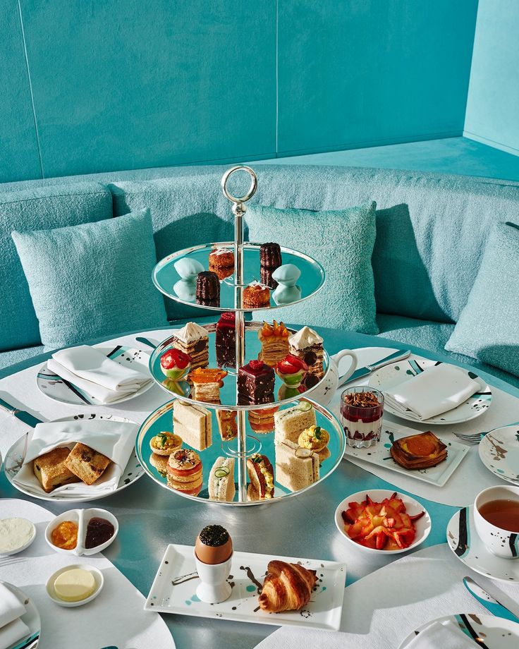 a table topped with plates and cups filled with food next to a blue couch covered in pillows