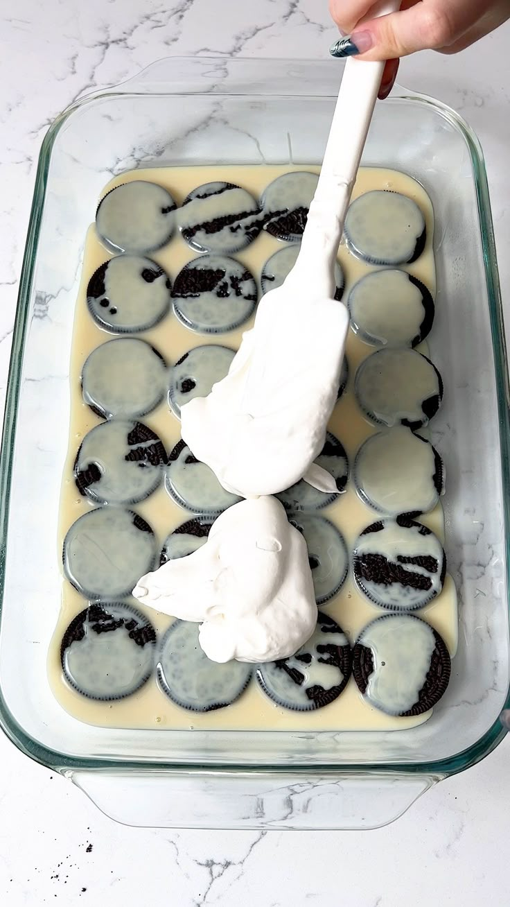 someone is spreading icing on top of cupcakes in a glass baking dish