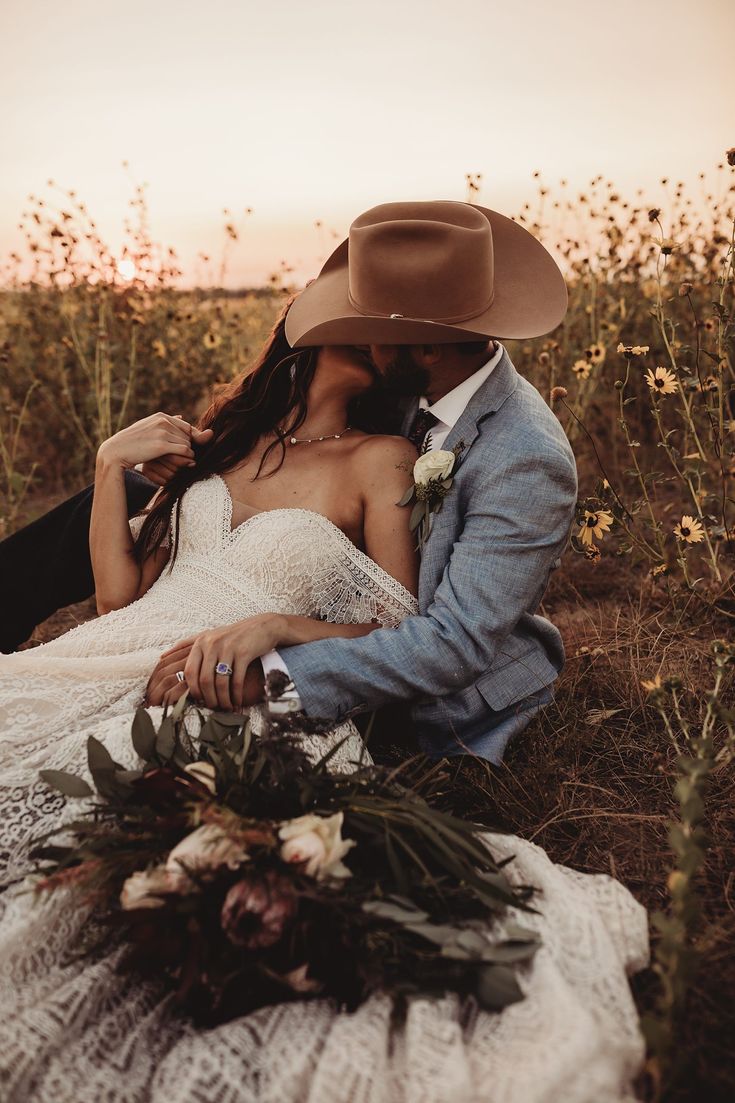 a man and woman sitting on the ground with flowers in front of their faces, wearing cowboy hats