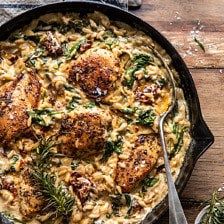 a skillet filled with pasta and meat on top of a wooden table next to silverware