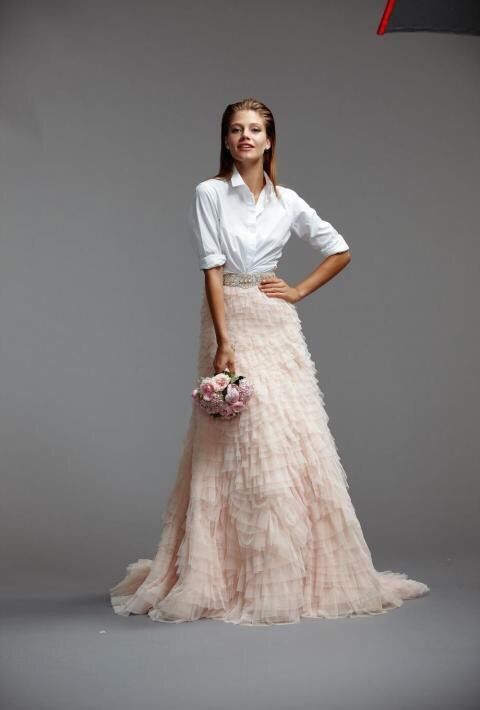 a woman in a white shirt and pink skirt holding a bouquet of flowers while standing against a gray background