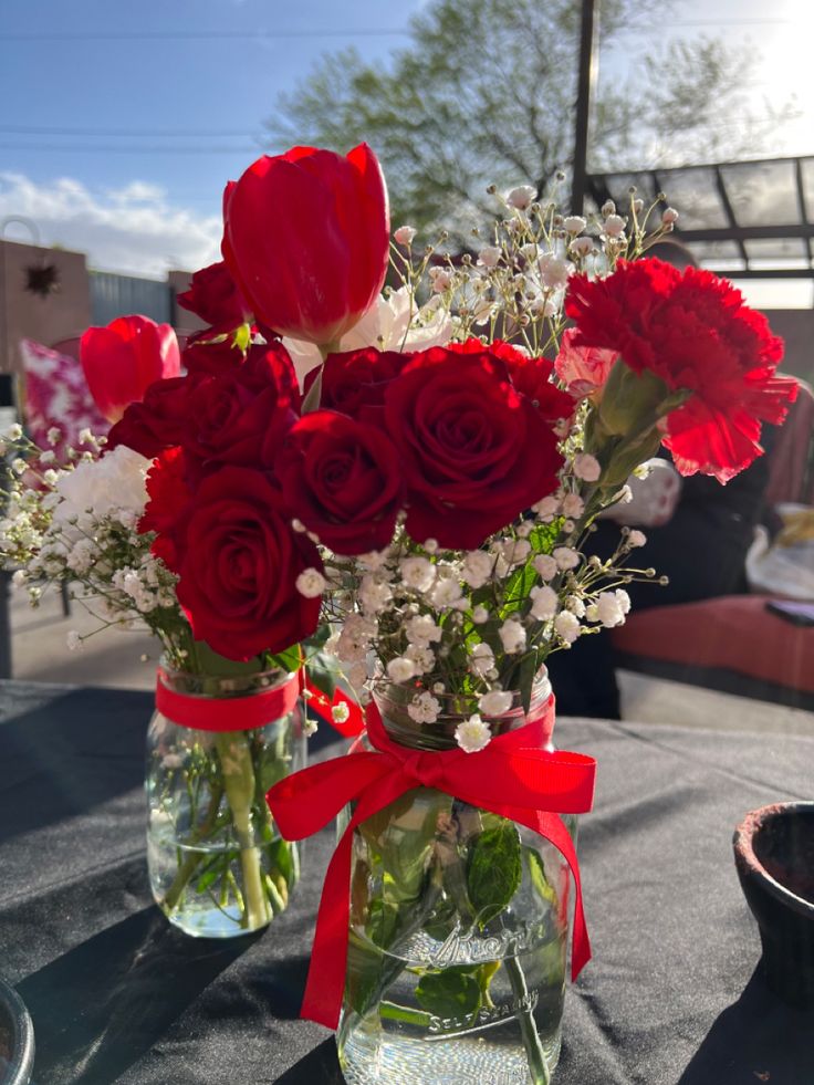 two vases filled with red and white flowers on top of a black table cloth