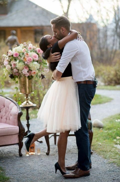 a man and woman embracing each other in front of a pink chair with flowers on it