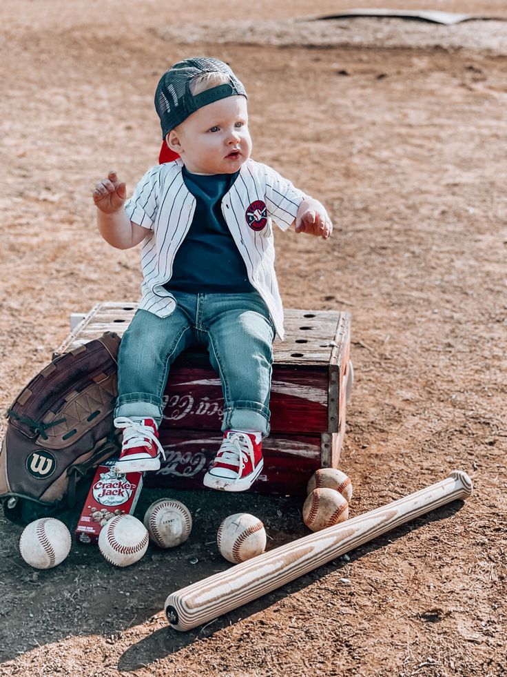 a young boy sitting on top of a wooden box with baseballs and bats around him