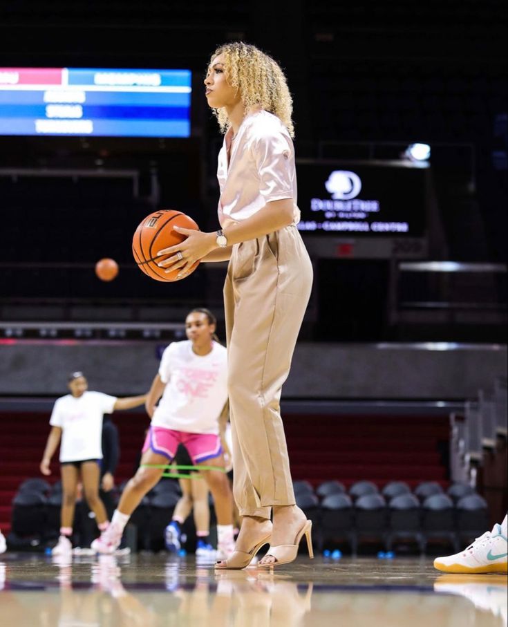 a woman holding a basketball while standing on top of a basketball court with other people