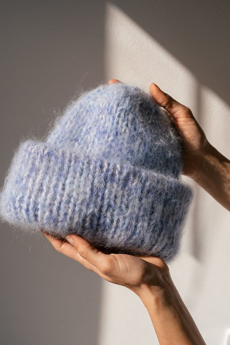 a hand holding a blue hat in front of a white wall