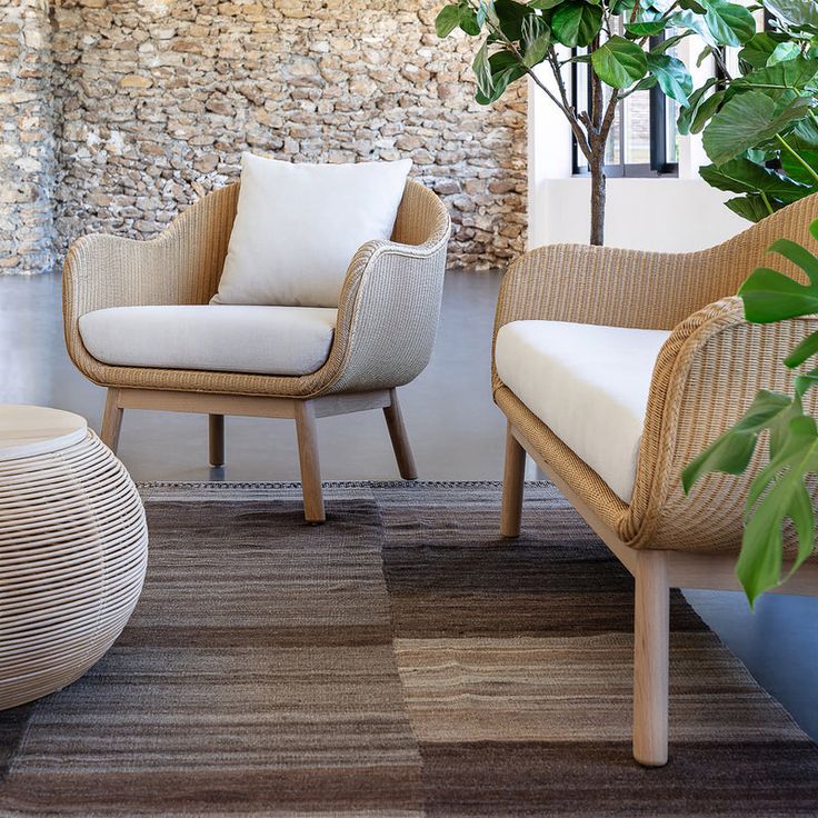 two wicker chairs sitting next to each other in front of a stone wall and potted plant