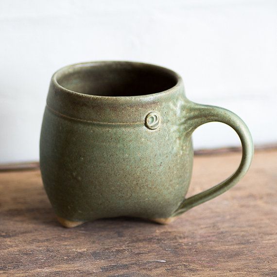 a green ceramic cup sitting on top of a wooden table next to a white wall