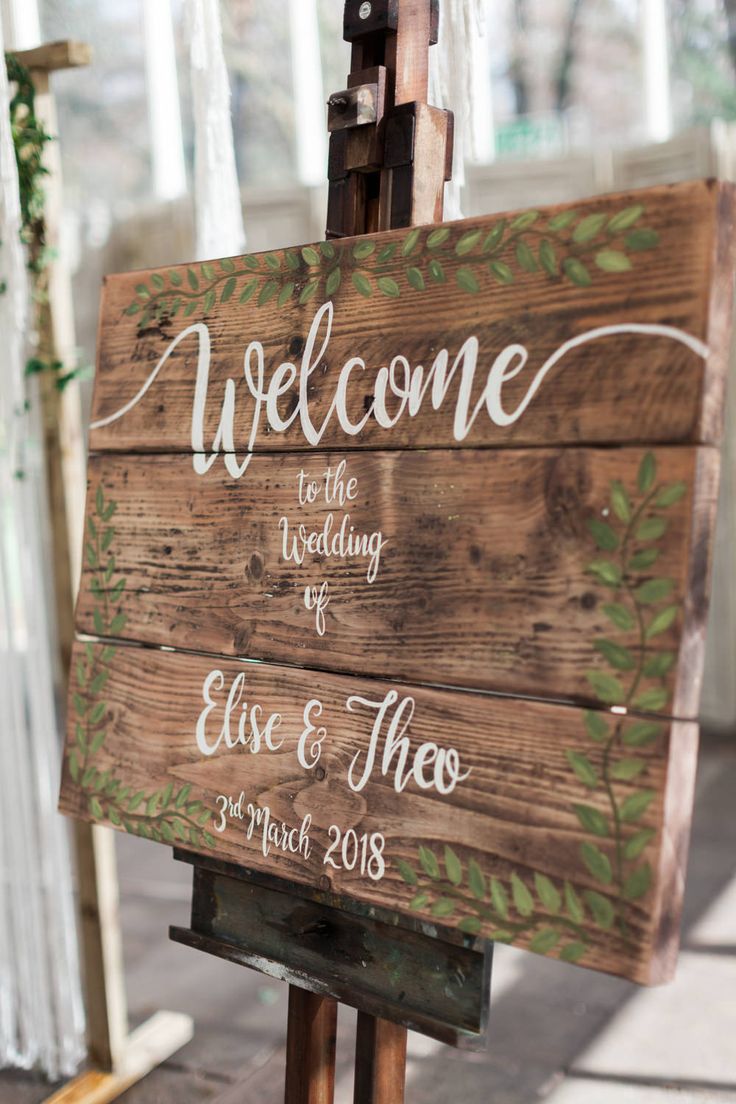 a wooden sign that says welcome to the wedding and also has greenery on it