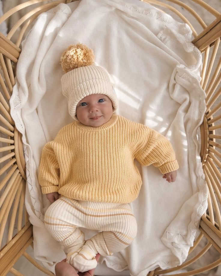 a baby in a yellow sweater and white pants is laying on a wicker chair