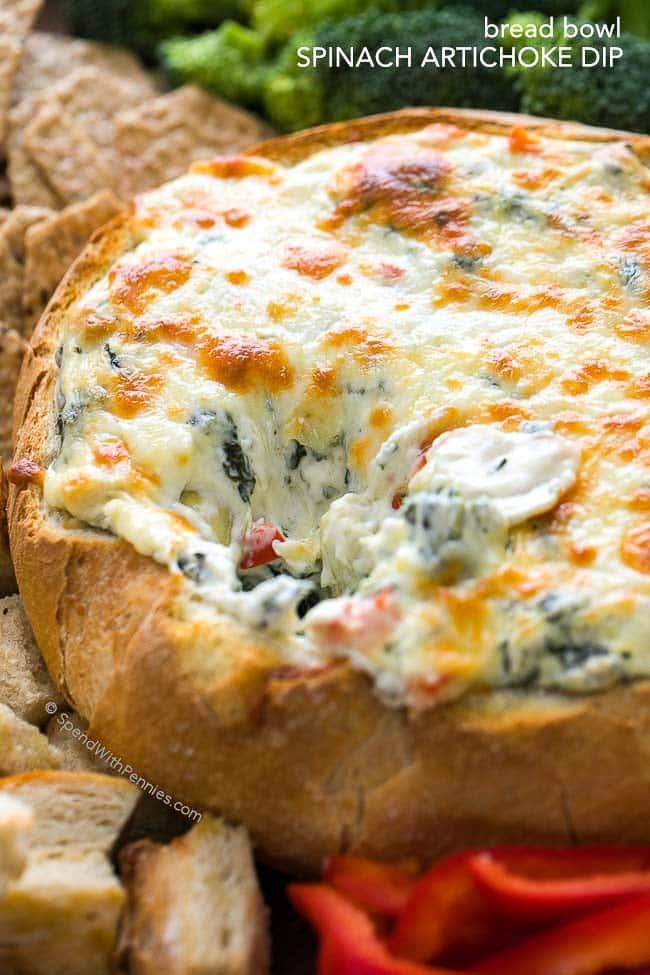 spinach artichoke dip in bread bowl surrounded by sliced vegetables and crackers