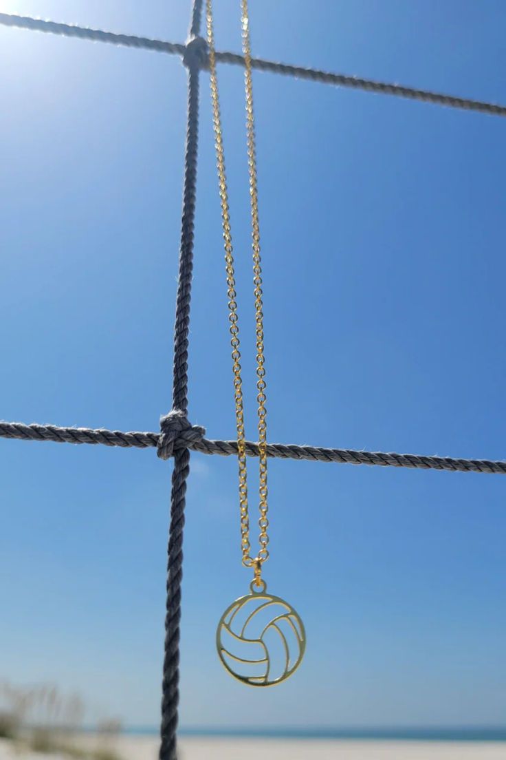 a volleyball ball is hanging from a chain on the beach with blue sky and water in the background