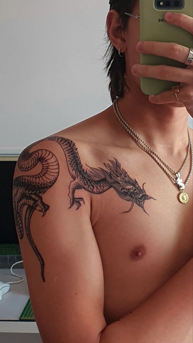 a shirtless man taking a selfie with his cell phone and dragon tattoo on his chest