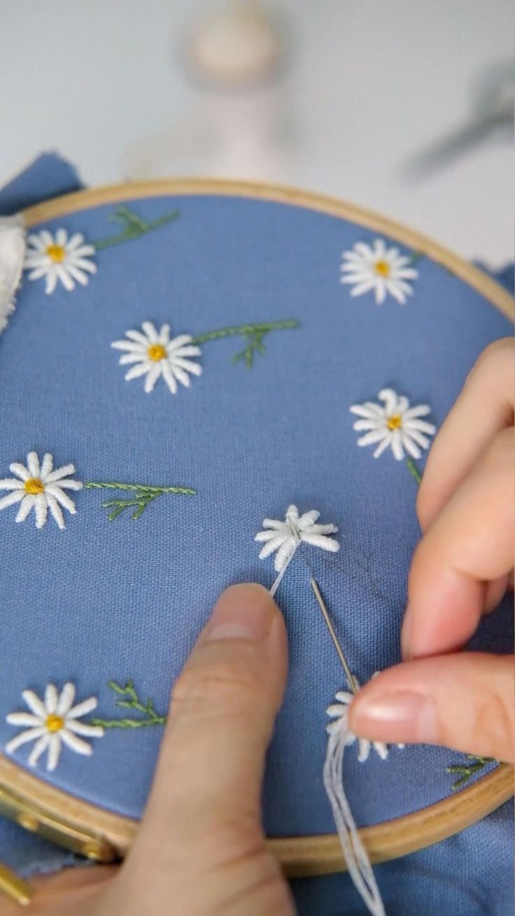 someone is stitching flowers on a blue cloth