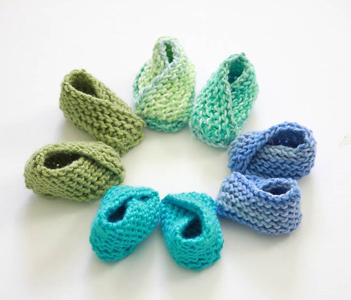 six knitted baby booties arranged in a circle on a white surface, with one blue and the other green