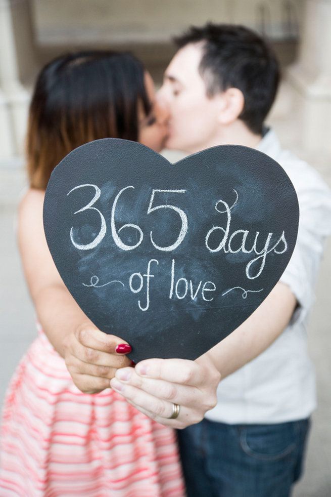 a man and woman kissing while holding a heart shaped chalkboard