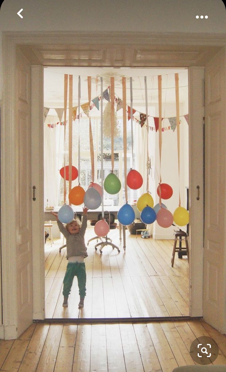 a young boy standing in front of an open door with balloons hanging from the ceiling